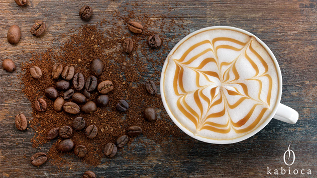 Tasse de capuccino avec latte art en forme de toile d'araignée, à côté de grains de café et café moulu